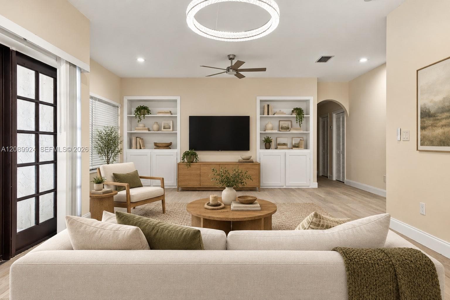 Living area featuring dual built-in floor-to-ceiling cabinetry, wood-finish flooring, circular LED chandelier, ceiling fan, and glass-paned French doors