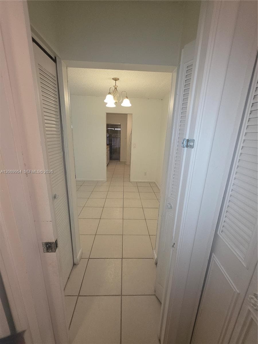 Stacked white laundry appliance with top-loading washer and front-loading dryer, situated within a dedicated alcove featuring tiled flooring