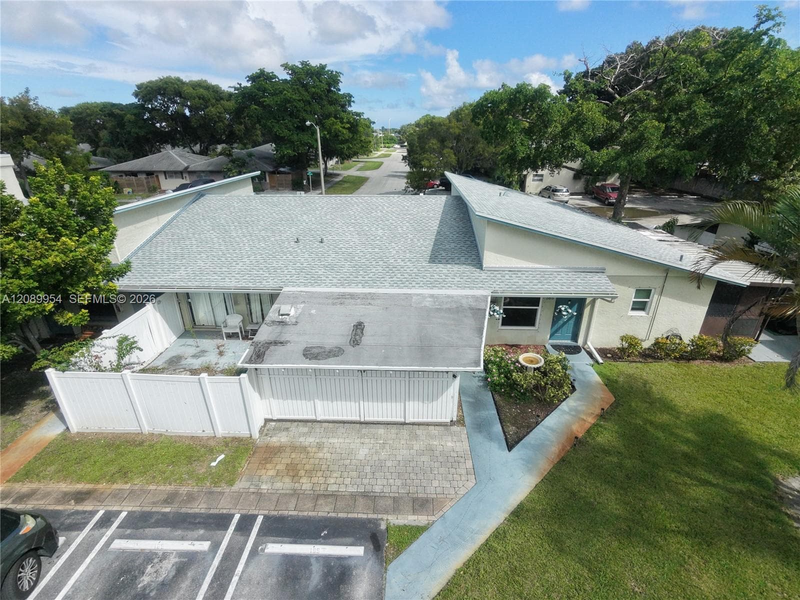 Single-story residence featuring a shingle roof, paved driveway, enclosed outdoor patio area, and white vinyl perimeter fencing