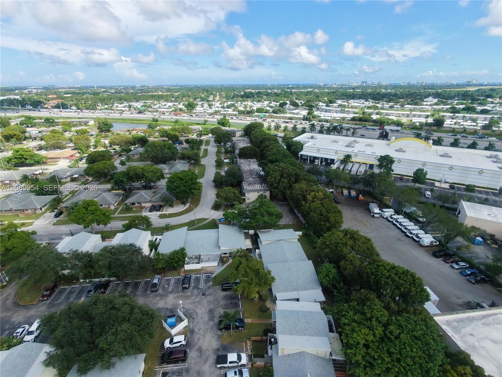 Aerial perspective featuring multi-unit structures with shingle roofing, paved surface parking, and mature tree canopy throughout the grounds