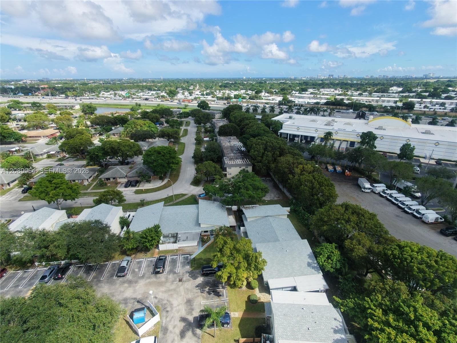 Aerial perspective of the residential complex featuring shingled roofs, asphalt parking areas, and mature tree canopy throughout the grounds