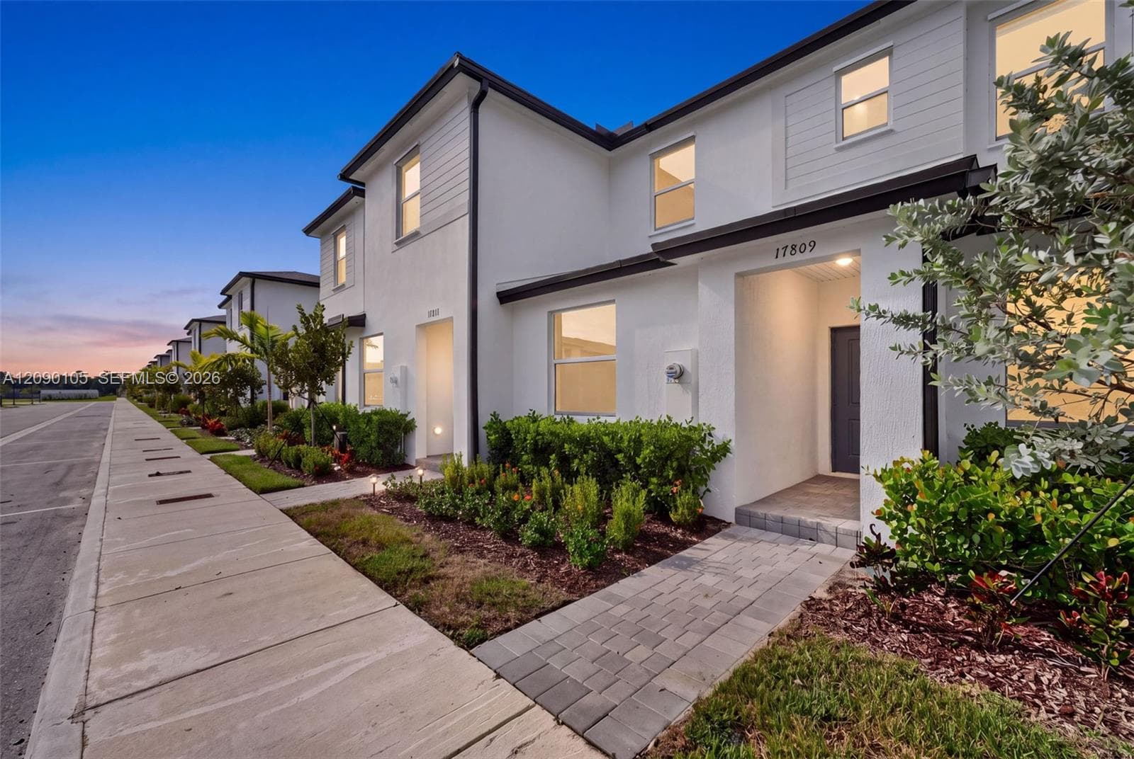 Two-story stucco exterior featuring horizontal siding accents, dark-framed windows, recessed entryways, and paver walkways