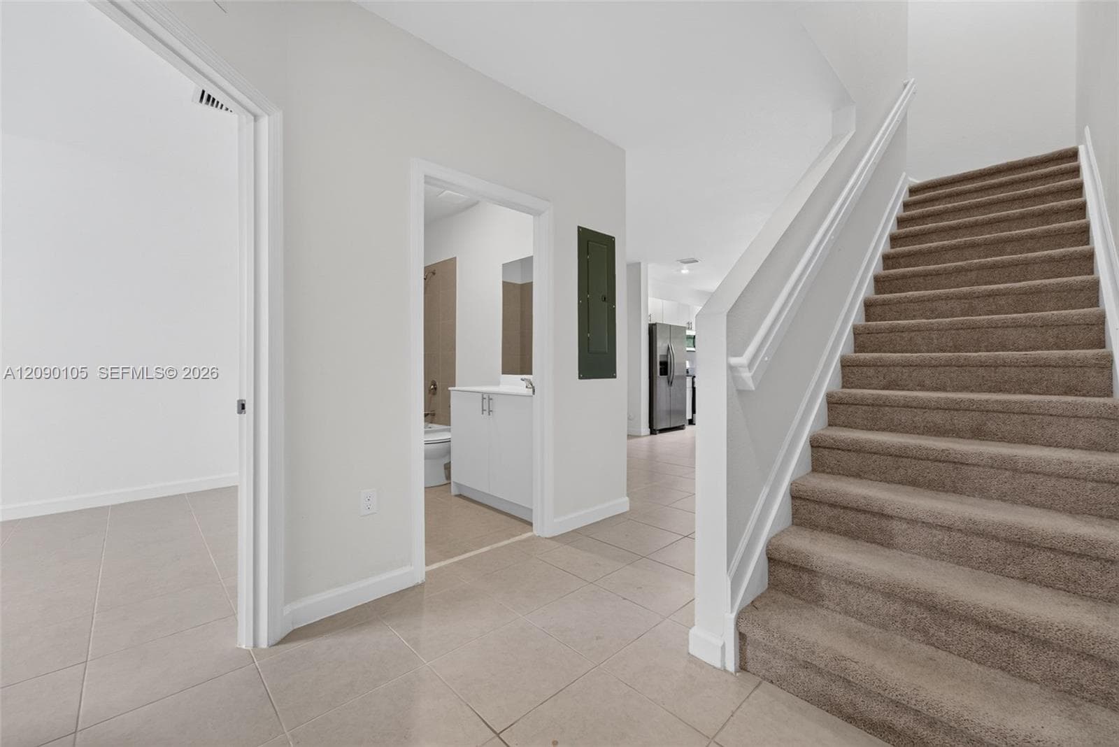Foyer featuring large-format ceramic tile flooring, a carpeted staircase with white handrails, and a vanity with a white basin and cabinet