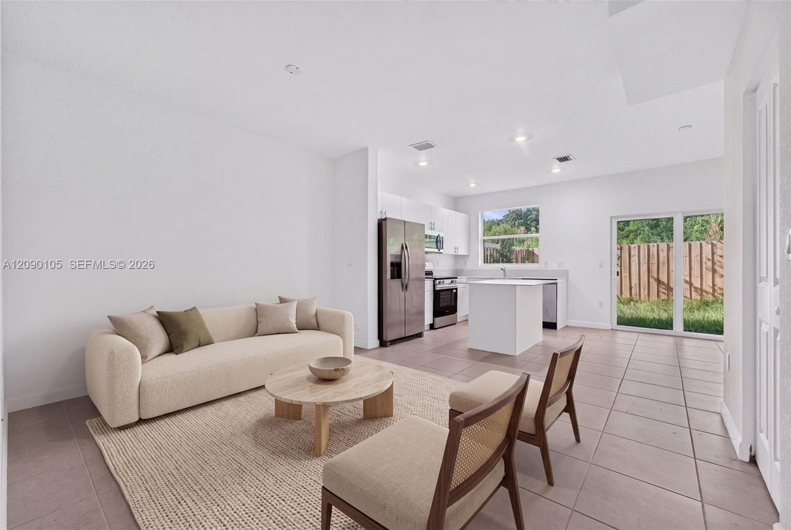 Open-concept interior featuring large-format ceramic tile flooring, a kitchen with white cabinetry and a central island, stainless steel appliances, recessed lighting, and sliding glass doors