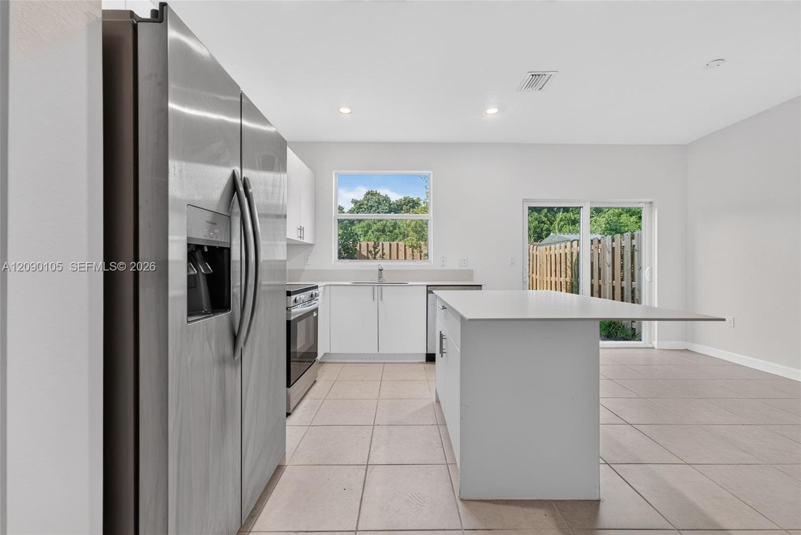 Kitchen featuring stainless steel refrigerator, white cabinetry, central island with countertop extension, recessed lighting, and tile flooring