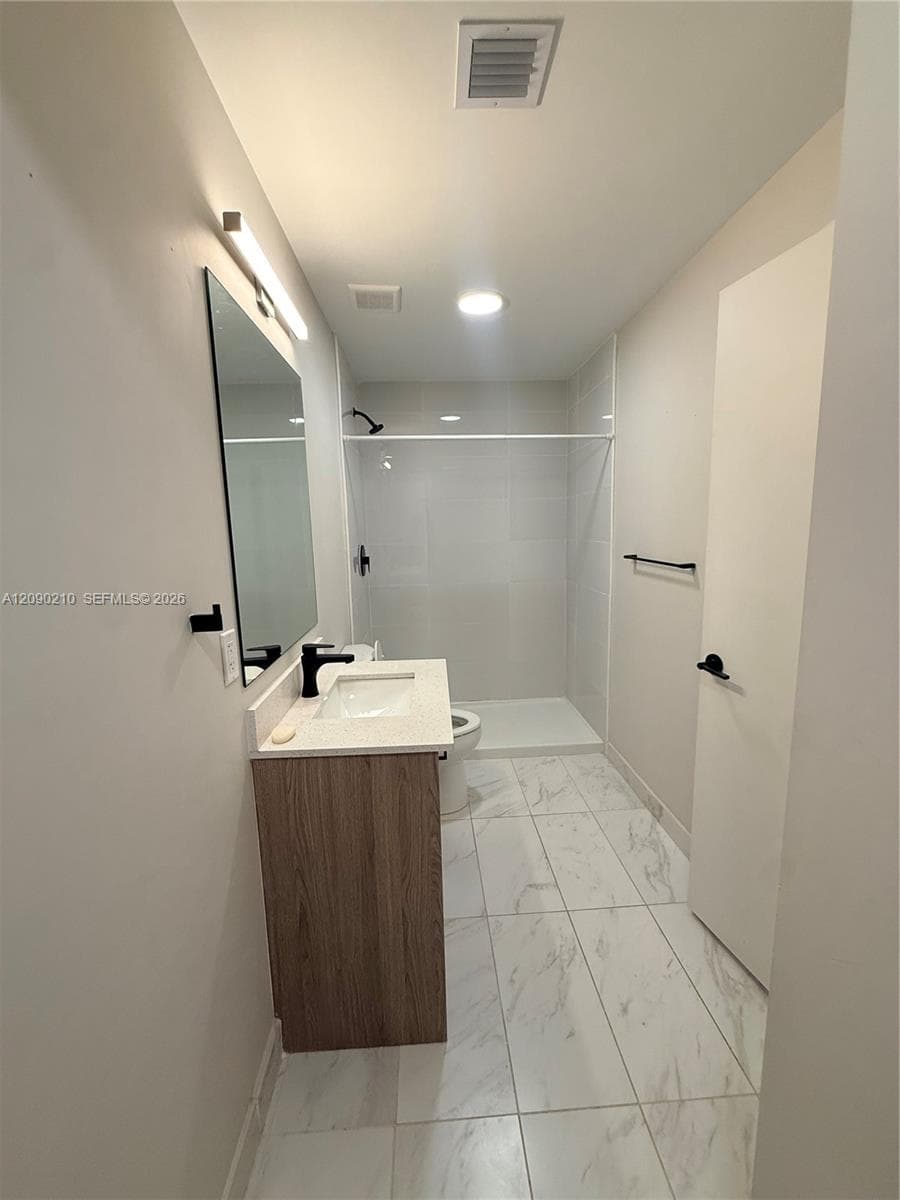 Bathroom featuring a wood-finish vanity with a stone-composite countertop, rectangular undermount sink, matte black faucet, and porcelain tile flooring with a veined pattern