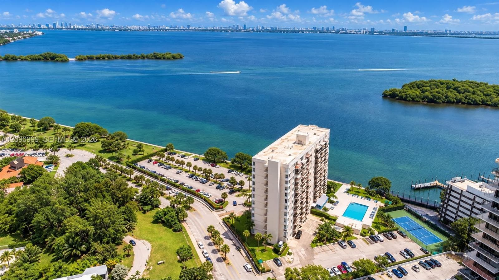 Aerial perspective of a high-rise building featuring a swimming pool, tennis court, surface parking, and water frontage