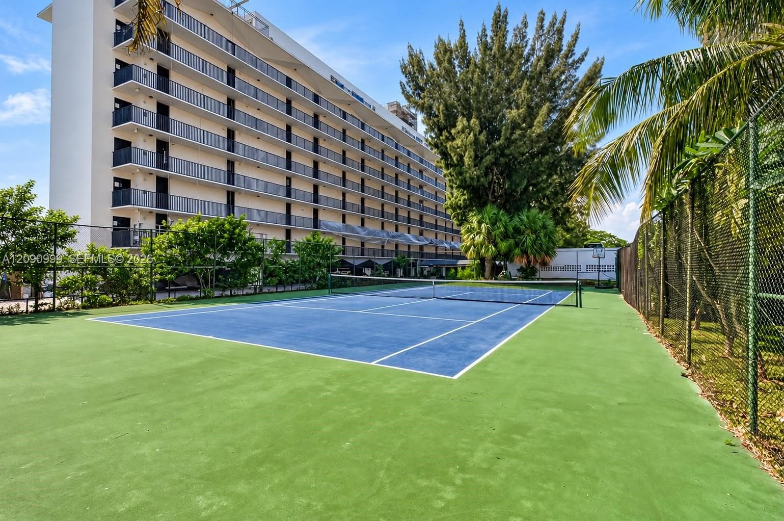 Tennis court featuring a hard surface, perimeter chain-link fencing, and mature surrounding landscaping