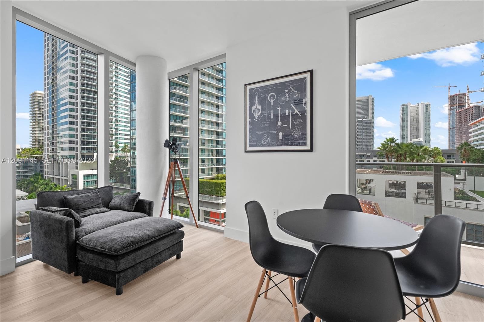 Expansive floor-to-ceiling windows, light wood-finish flooring, white walls, and a private balcony with a glass railing