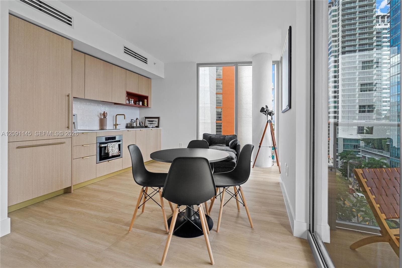 Integrated kitchen cabinetry with recessed appliances, wood-finish flooring, a built-in oven, a flat-panel range hood, and a ceiling-mounted linear air diffuser