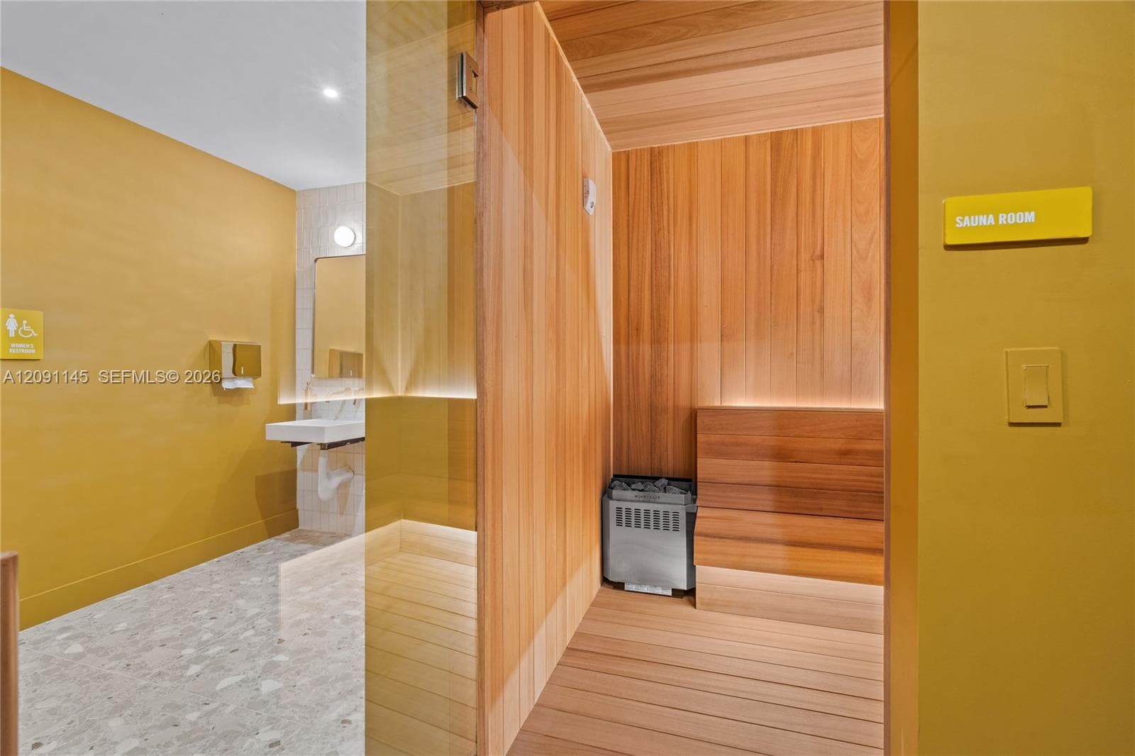 Sauna room featuring wood-paneled walls and bench, with a stone-fill electric heater
