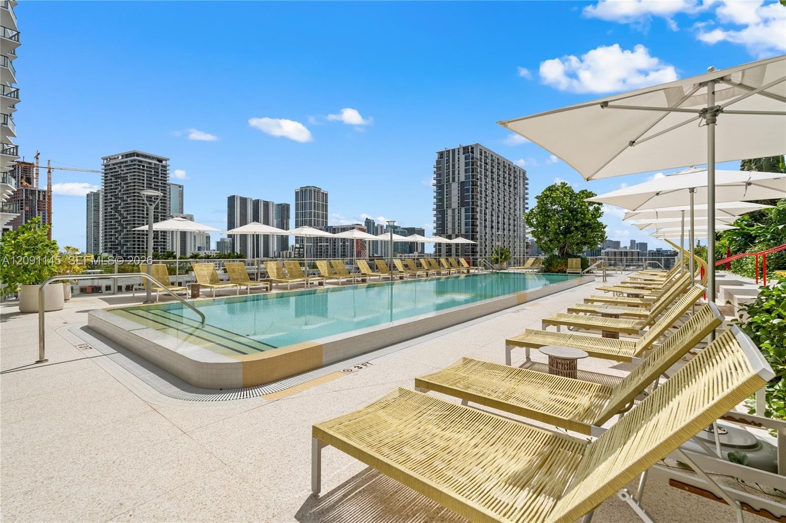 Rooftop pool deck featuring an in-ground swimming pool, multiple lounge chairs, shade umbrellas, and a city skyline backdrop