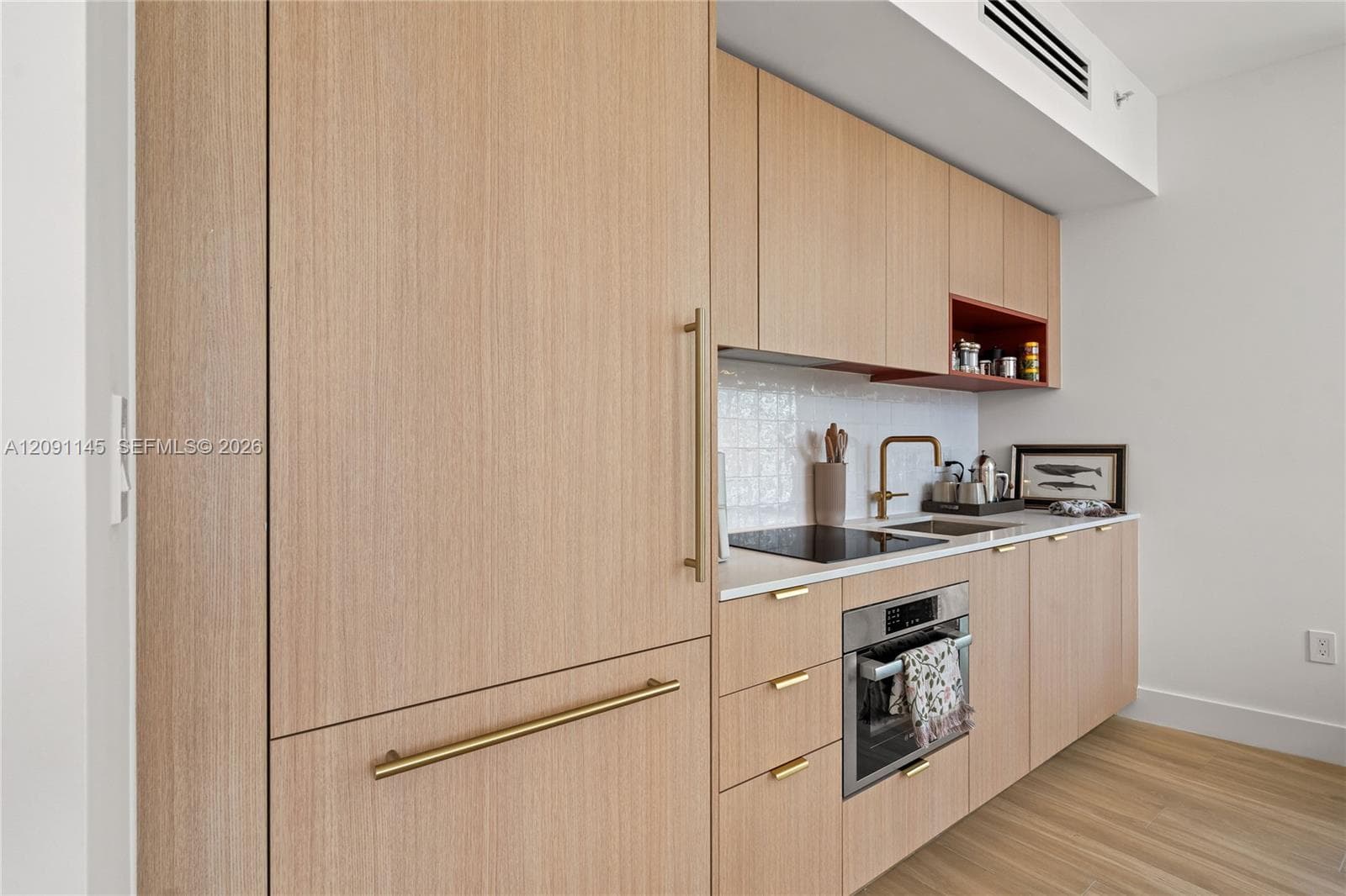 Light wood-finish cabinetry with integrated appliances, white countertop, and white tile backsplash