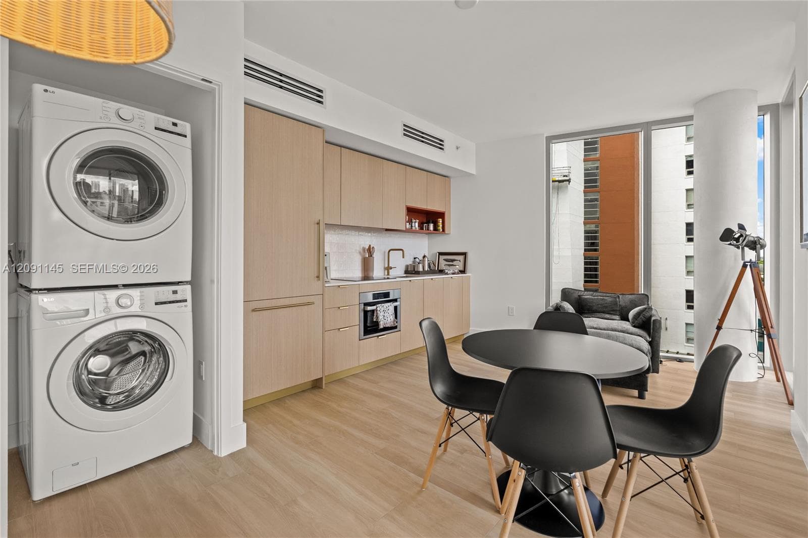 Integrated kitchen with light wood-finish cabinetry, built-in appliances, and a stacked washer and dryer