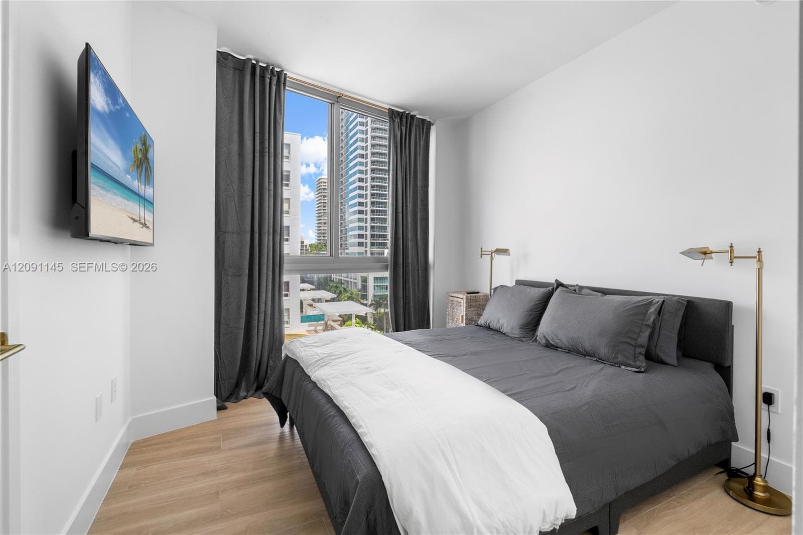 Expansive window with urban scenery, wood-finish flooring, white walls, and a wall-mounted television