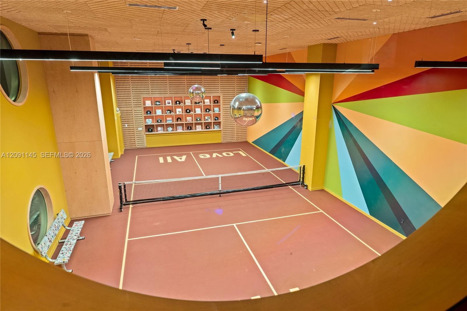 Indoor court with a net, geometric wall art, circular windows, and a built-in display shelf