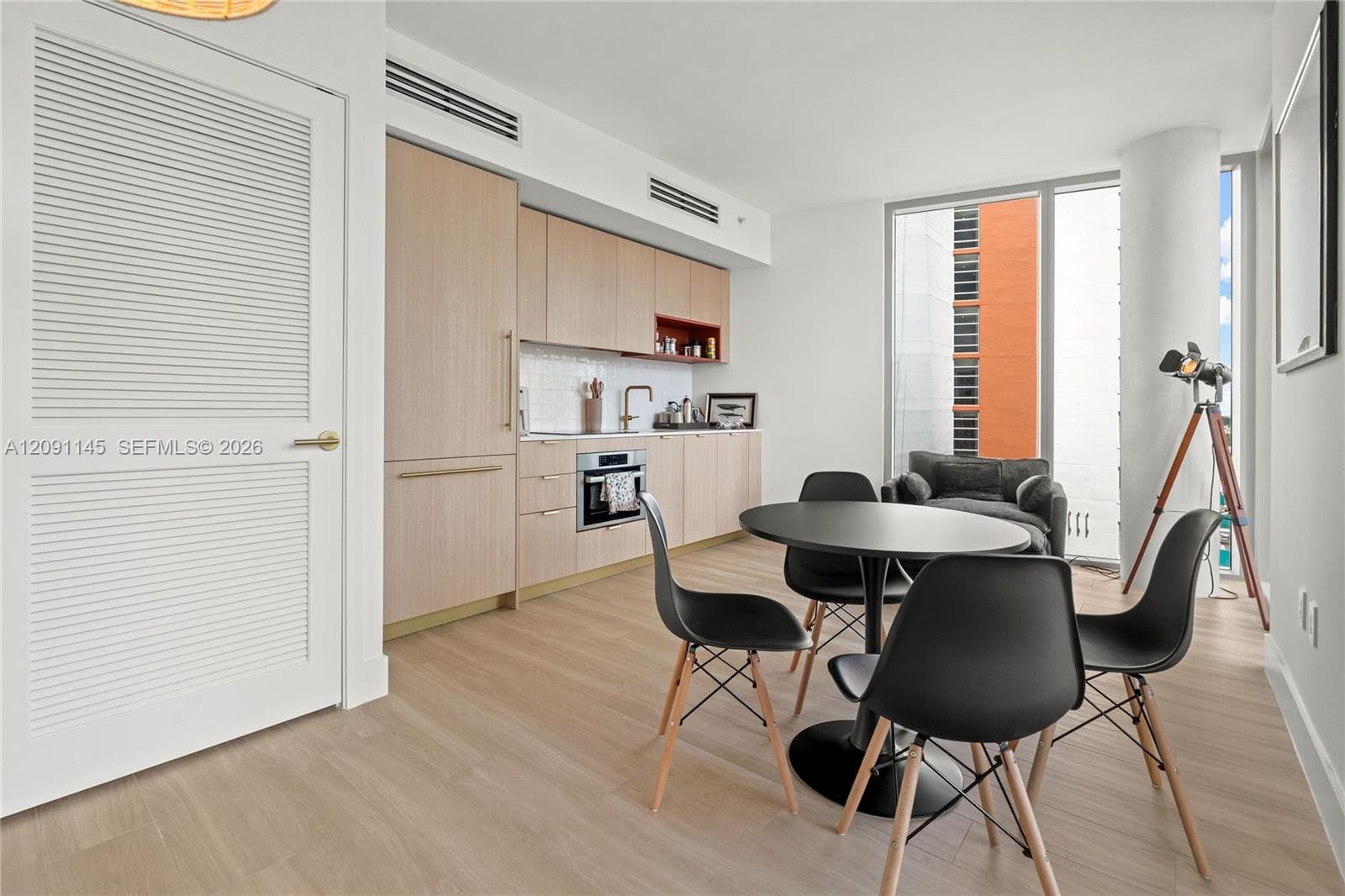 Light wood-finish flooring with a modern kitchen featuring wood cabinetry, integrated appliances, and a tiled backsplash