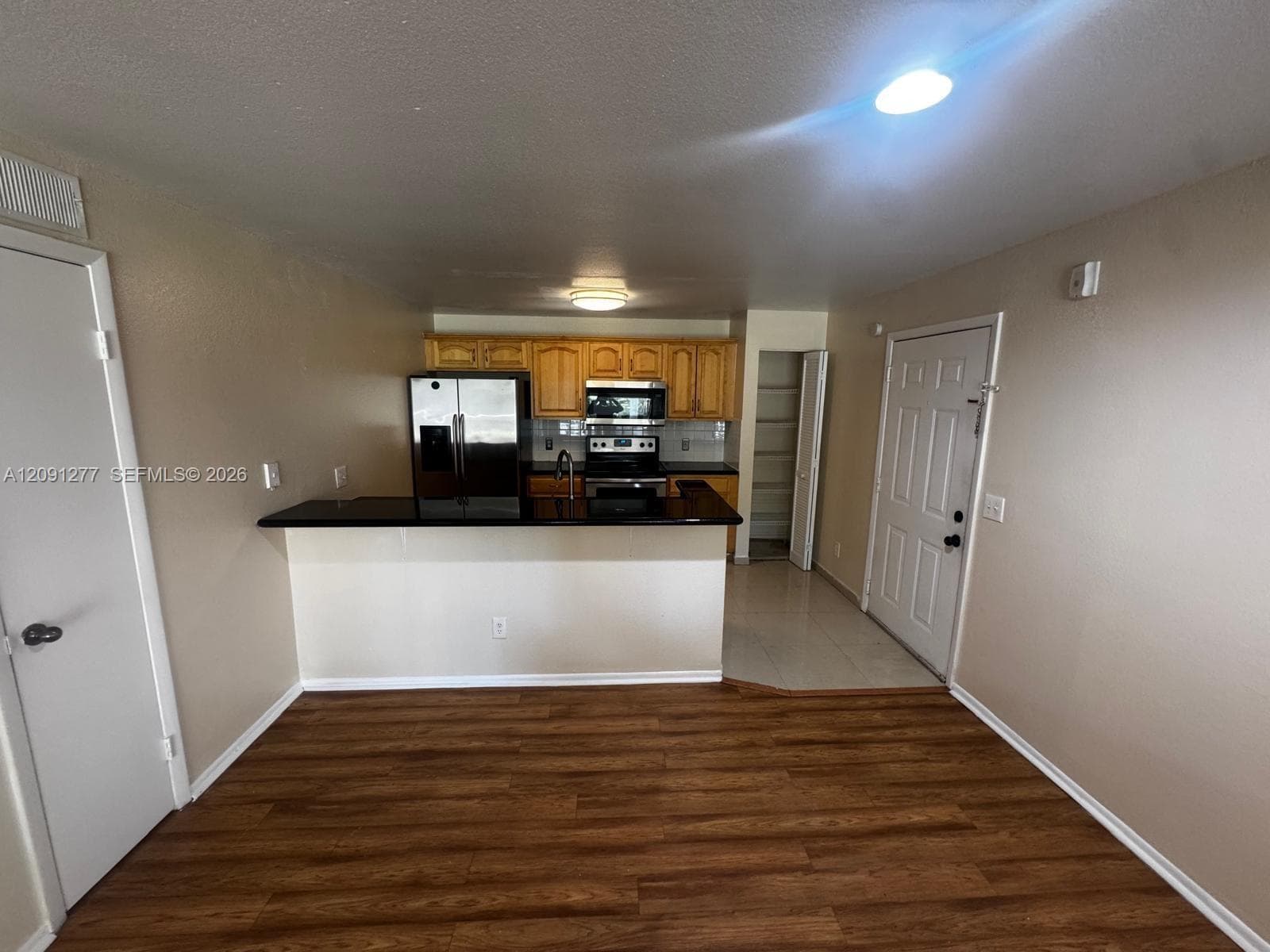 Kitchen featuring wood cabinetry, dark countertops, built-in stainless steel appliances, a peninsula breakfast bar, and wood-finish flooring