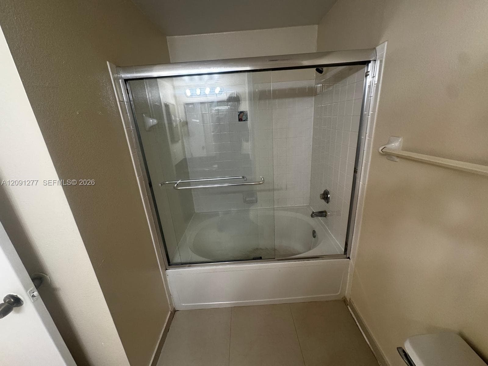 Bathtub and shower combination featuring a glass sliding door enclosure, white tile surround, and chrome hardware