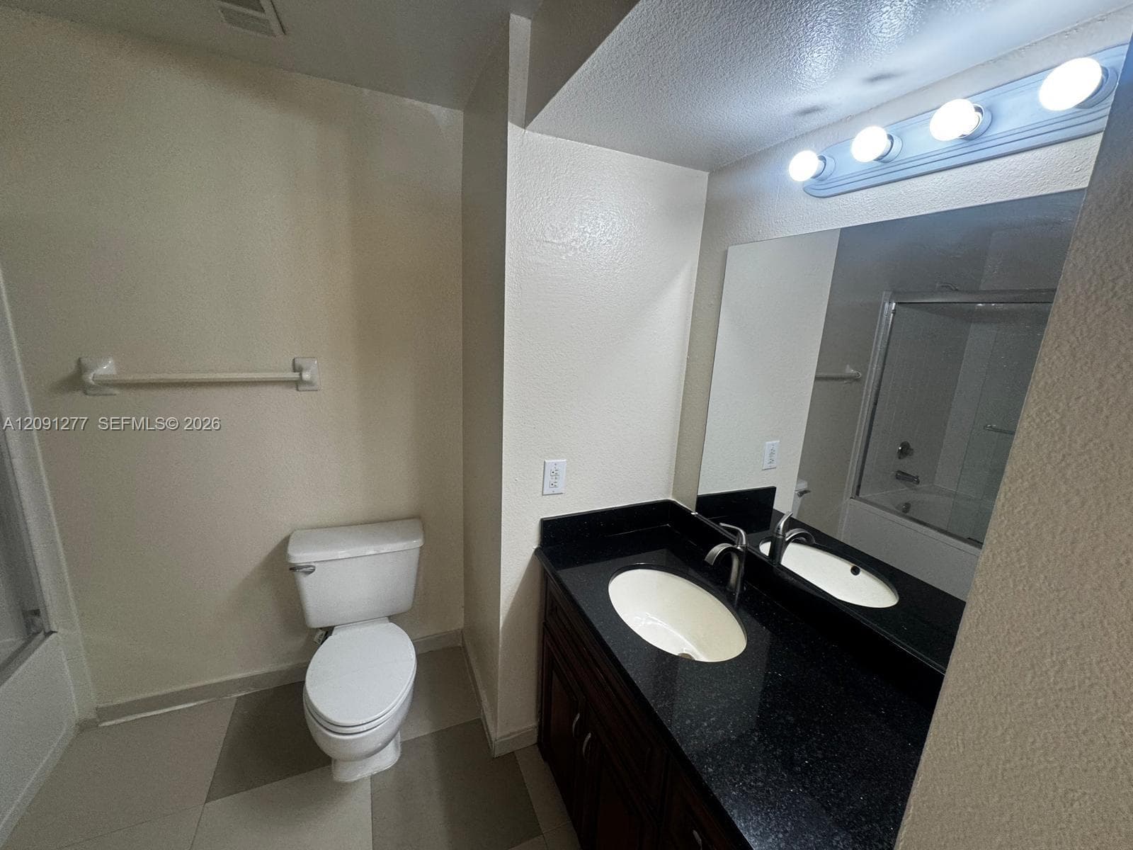 Bathroom featuring a vanity with dark stone countertop, undermount oval sink, dark wood-finish cabinetry, and three-bulb vanity light fixture