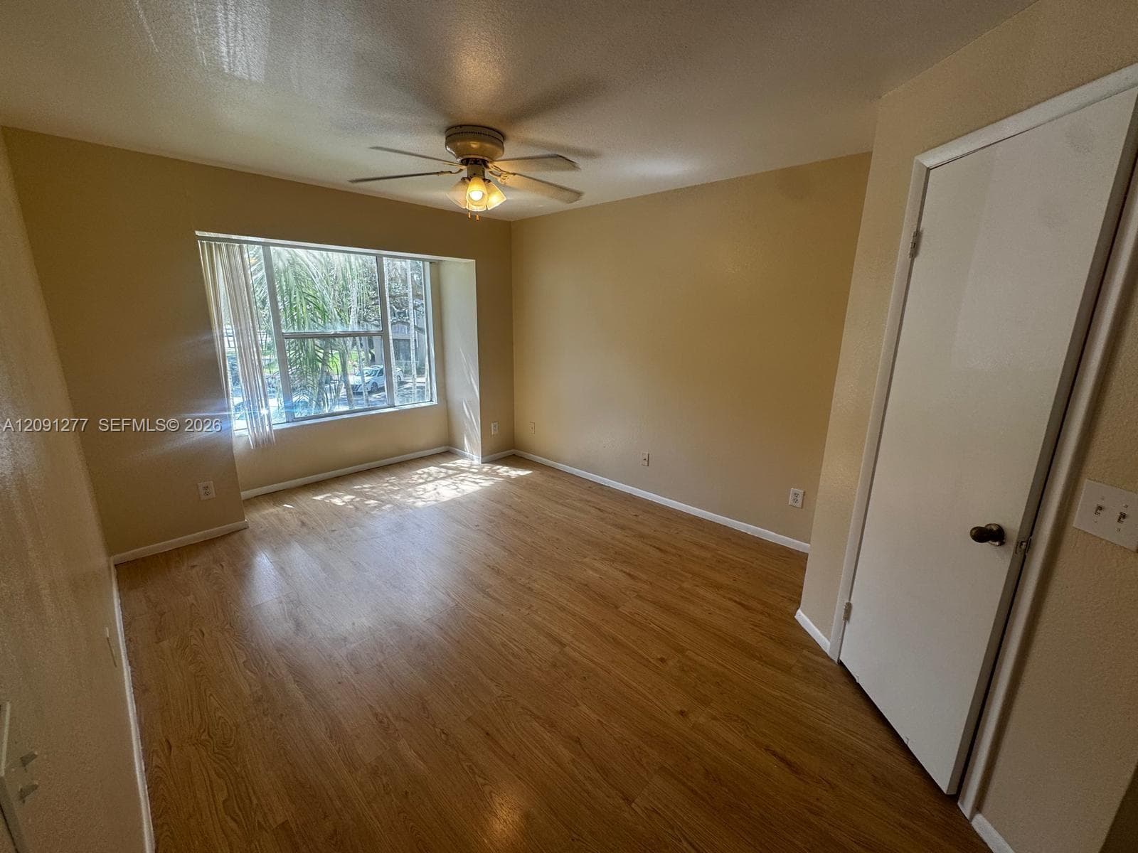 Interior room featuring wood-finish flooring, a multi-pane window, a ceiling fan with integrated light fixture, and a closet with a standard swing door