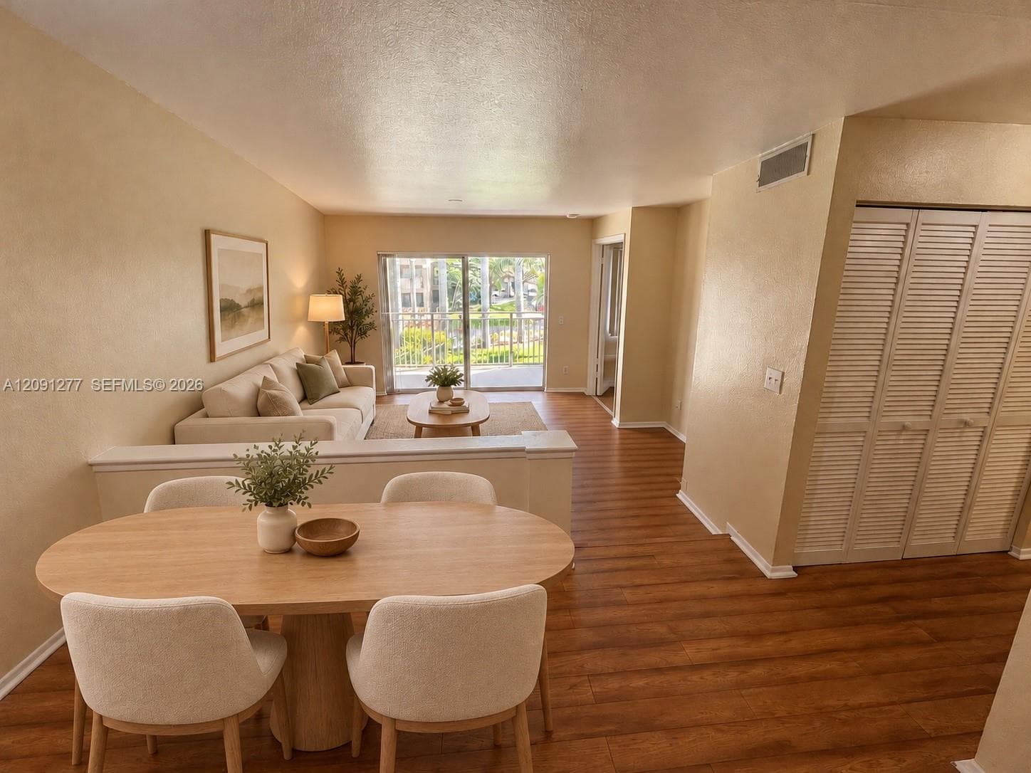 Living area featuring wood-finish flooring, half-wall divider, sliding glass door with exterior balcony access, and bifold louvered closet doors