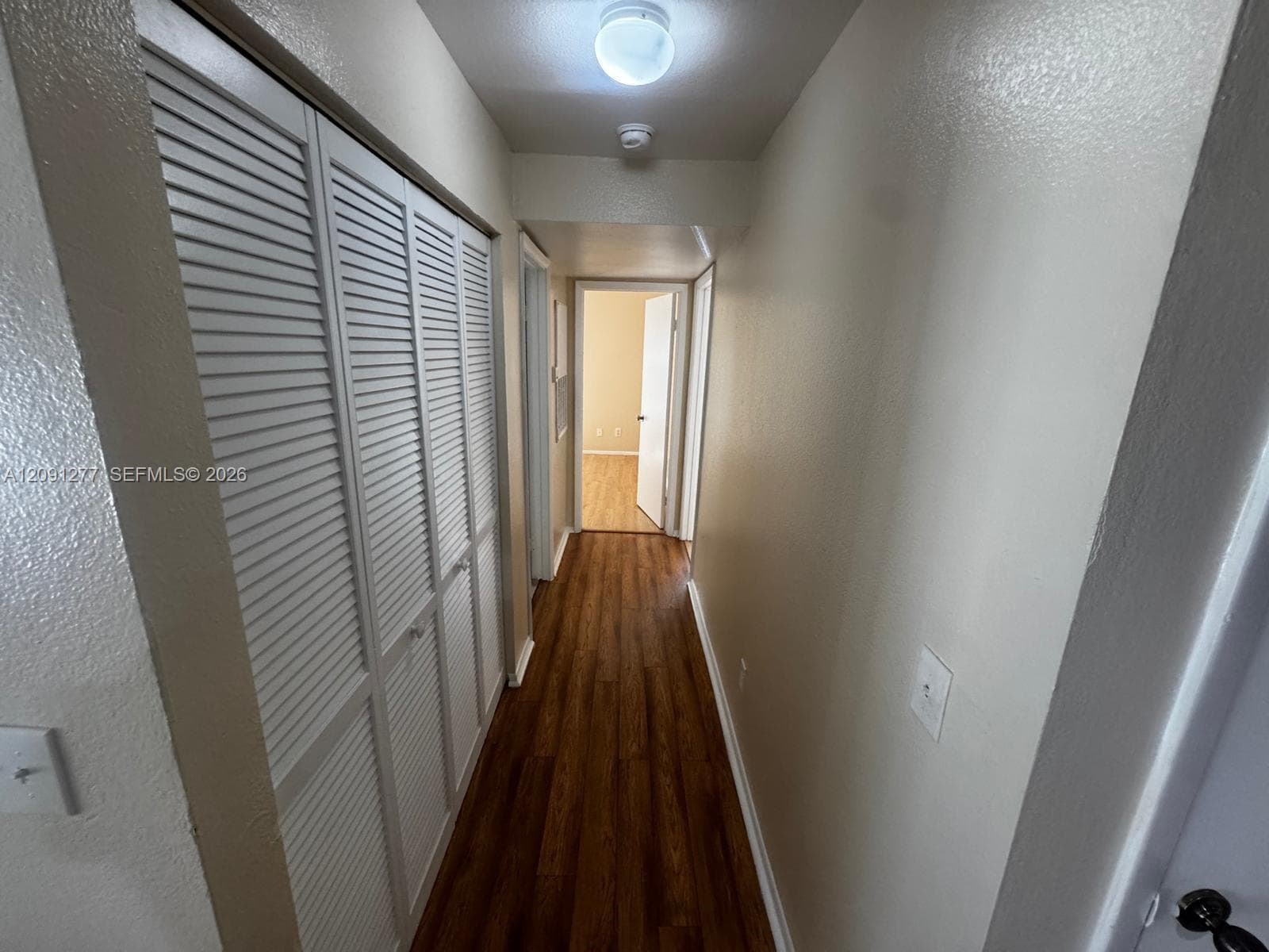 Hallway featuring wood-finish flooring, white louvered closet doors, and flush-mount lighting