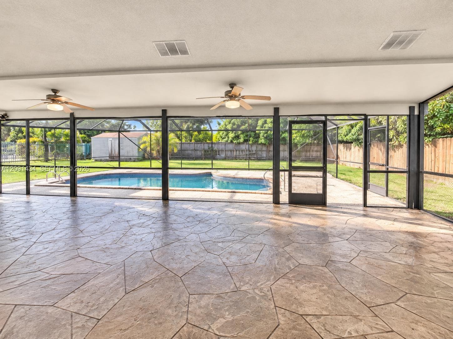 Screened-in lanai featuring stamped concrete flooring, dual ceiling fans, and a private pool