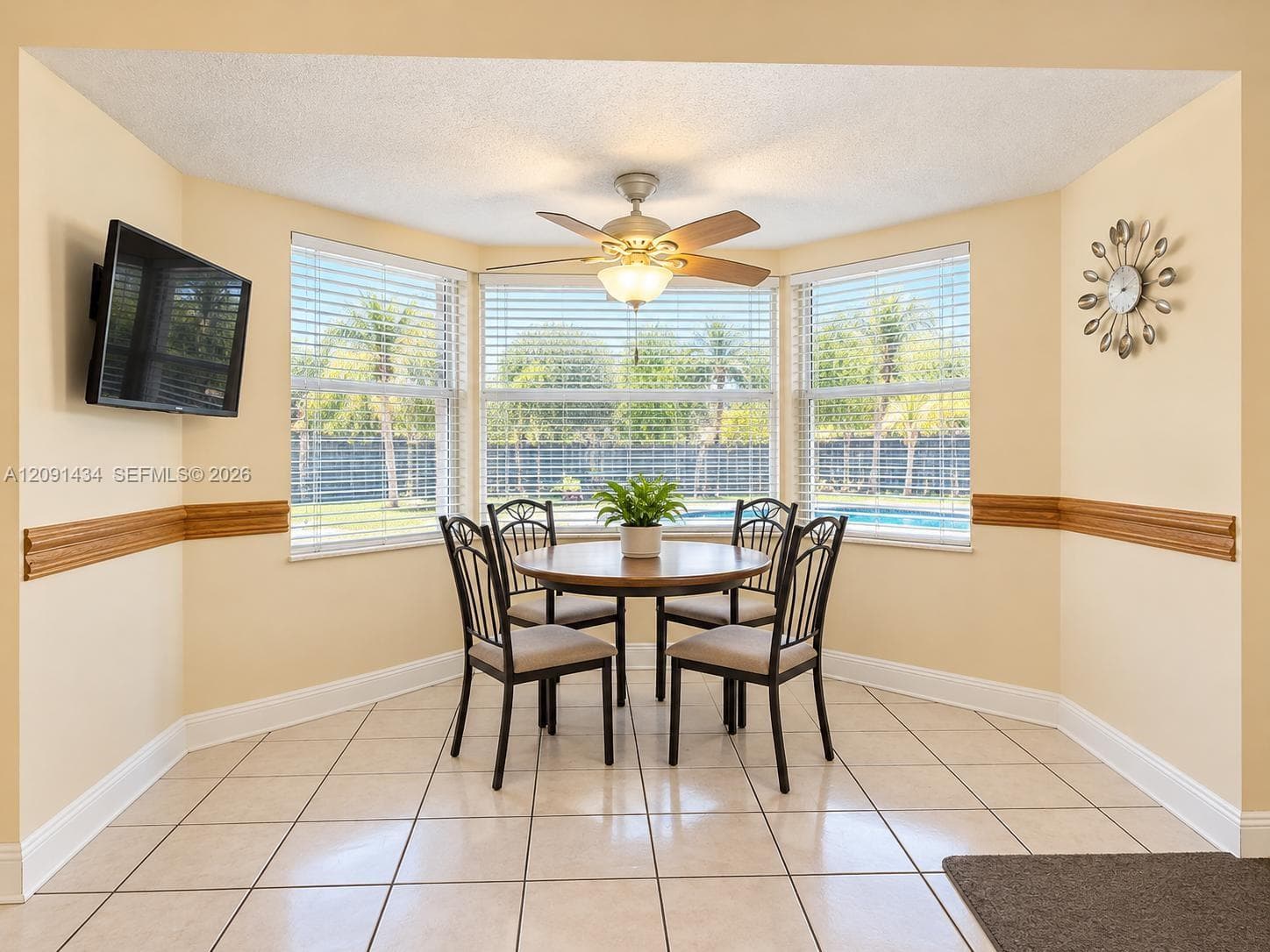 Bay window with three-panel glazing, neutral tile flooring, chair rail molding, and a central ceiling fan