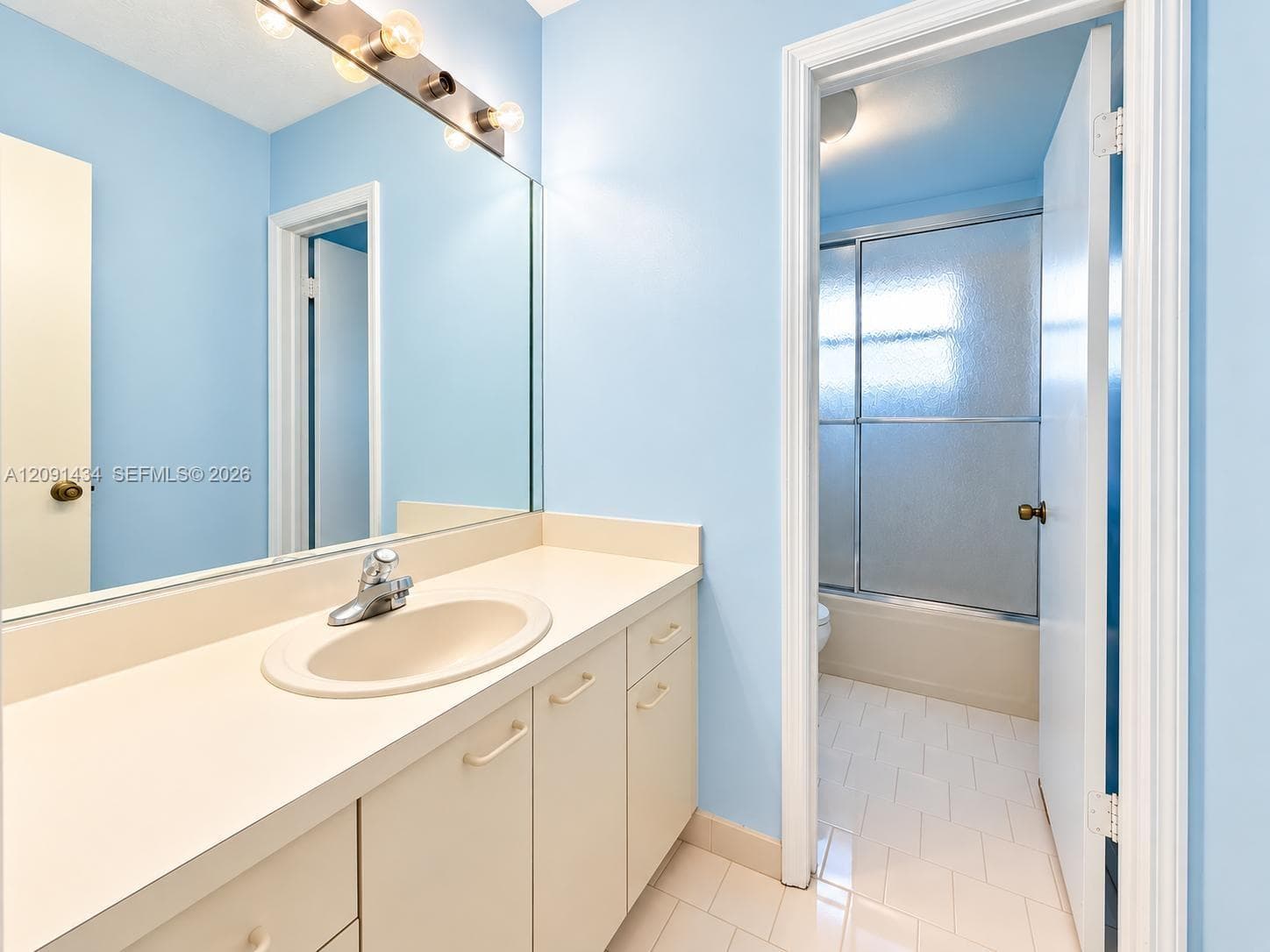 Bathroom vanity featuring a solid surface countertop with an integrated basin, multi-drawer cabinetry, a large wall-mounted mirror, and a multi-light fixture