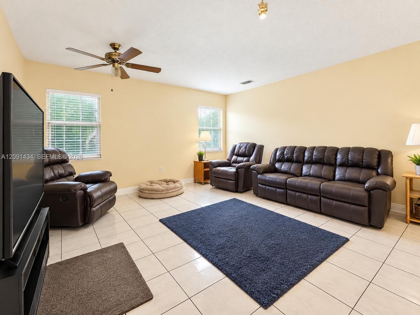 Neutral interior featuring large-format ceramic tile flooring, multi-pane windows with horizontal blinds, and a central ceiling fan