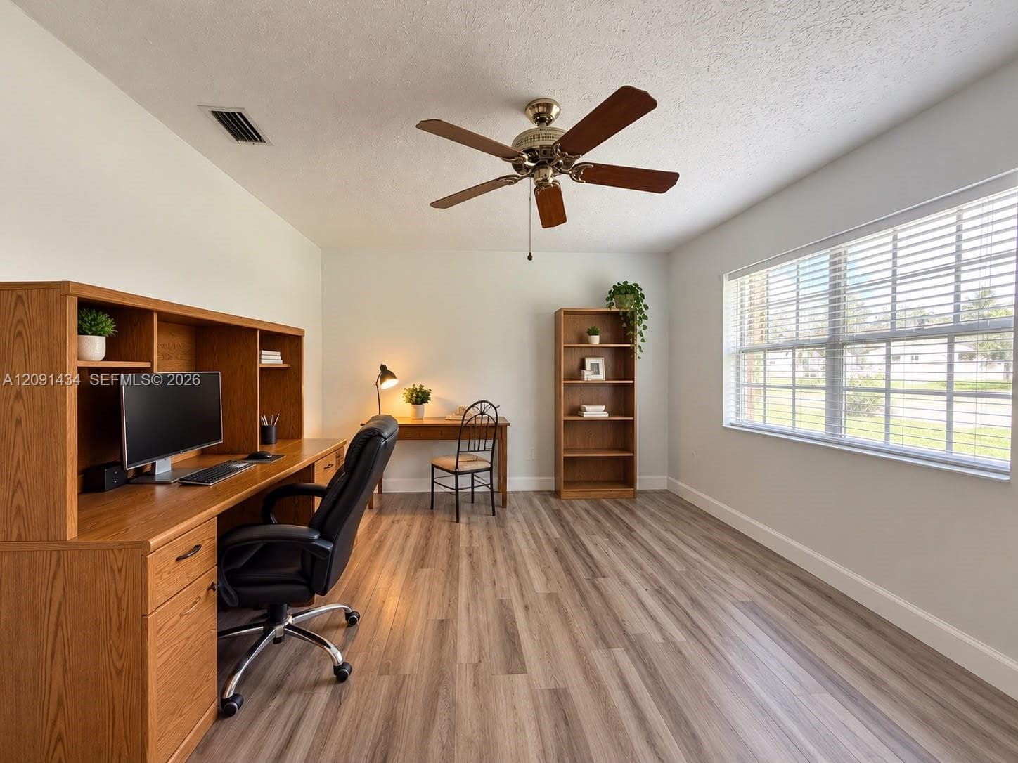 Room featuring wood-finish flooring, a ceiling fan with integrated lighting, and a large window with horizontal blinds