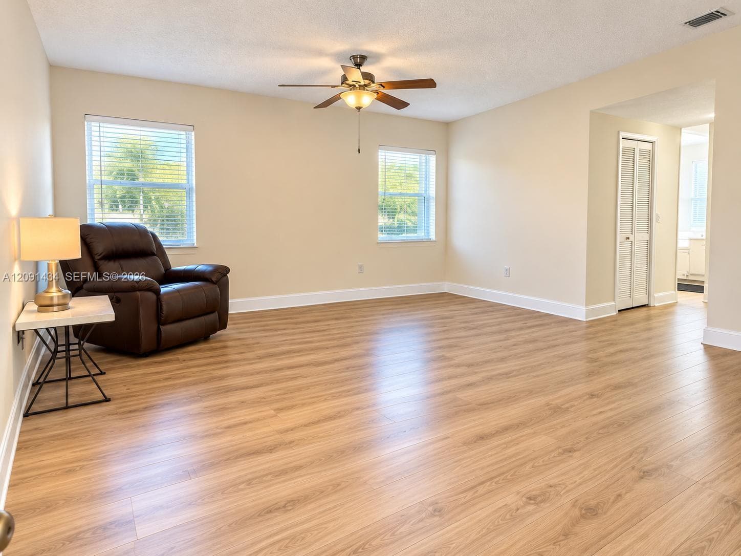 Neutral wall paint, wood-finish flooring, two large windows with blinds, built-in ceiling fan with light fixture, and bi-fold closet doors