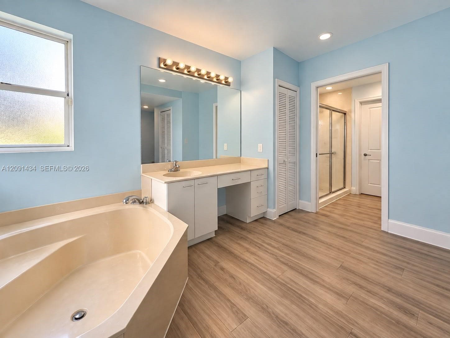 Bathroom featuring wood-finish flooring, a soaking tub with integrated deck, a vanity with a surface-mounted sink and large mirror, and a walk-in shower enclosure
