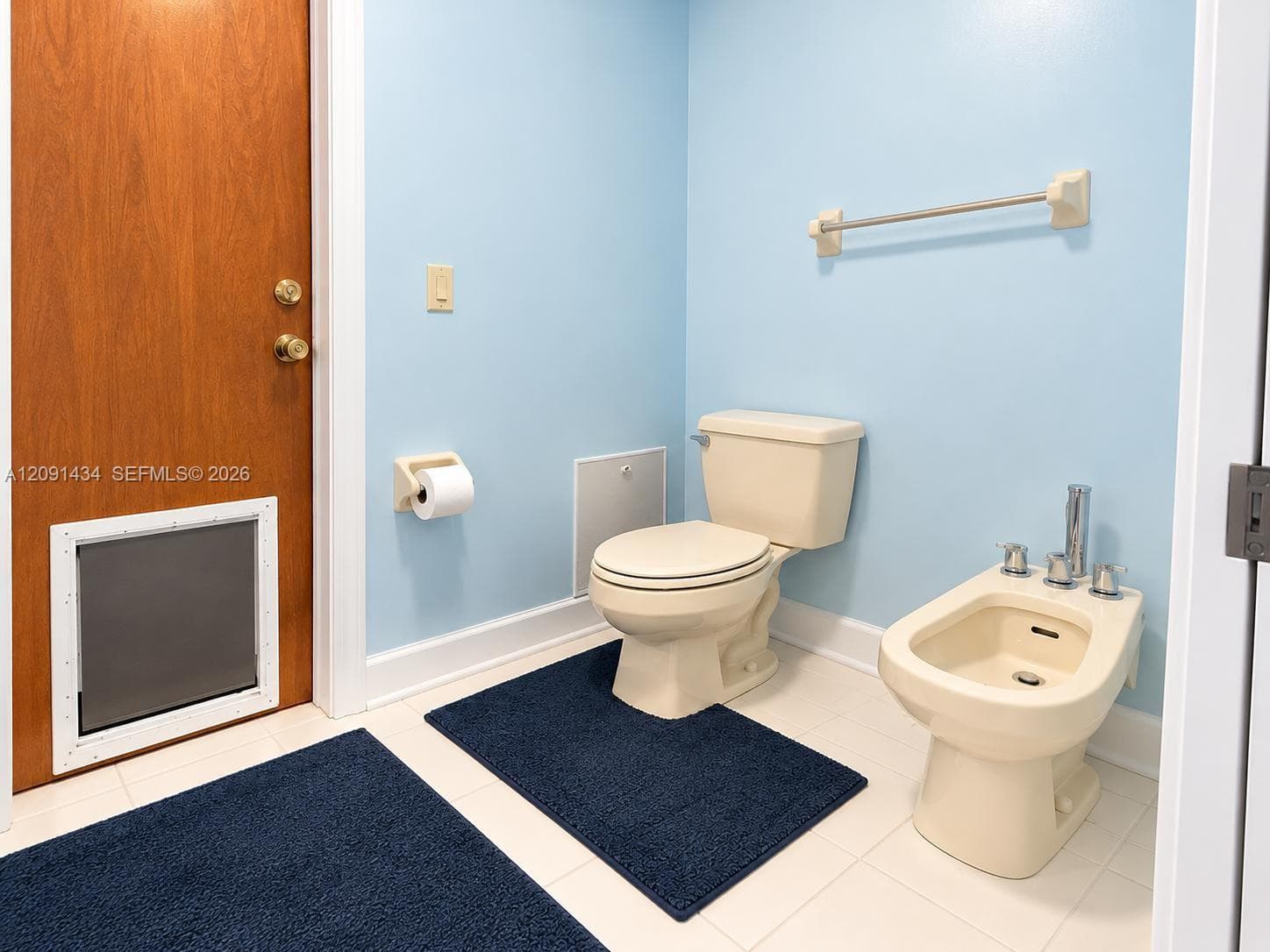 Bathroom featuring a two-piece commode, a floor-mounted bidet with chrome fixtures, a wood-finish door with an integrated pet door, and tile flooring