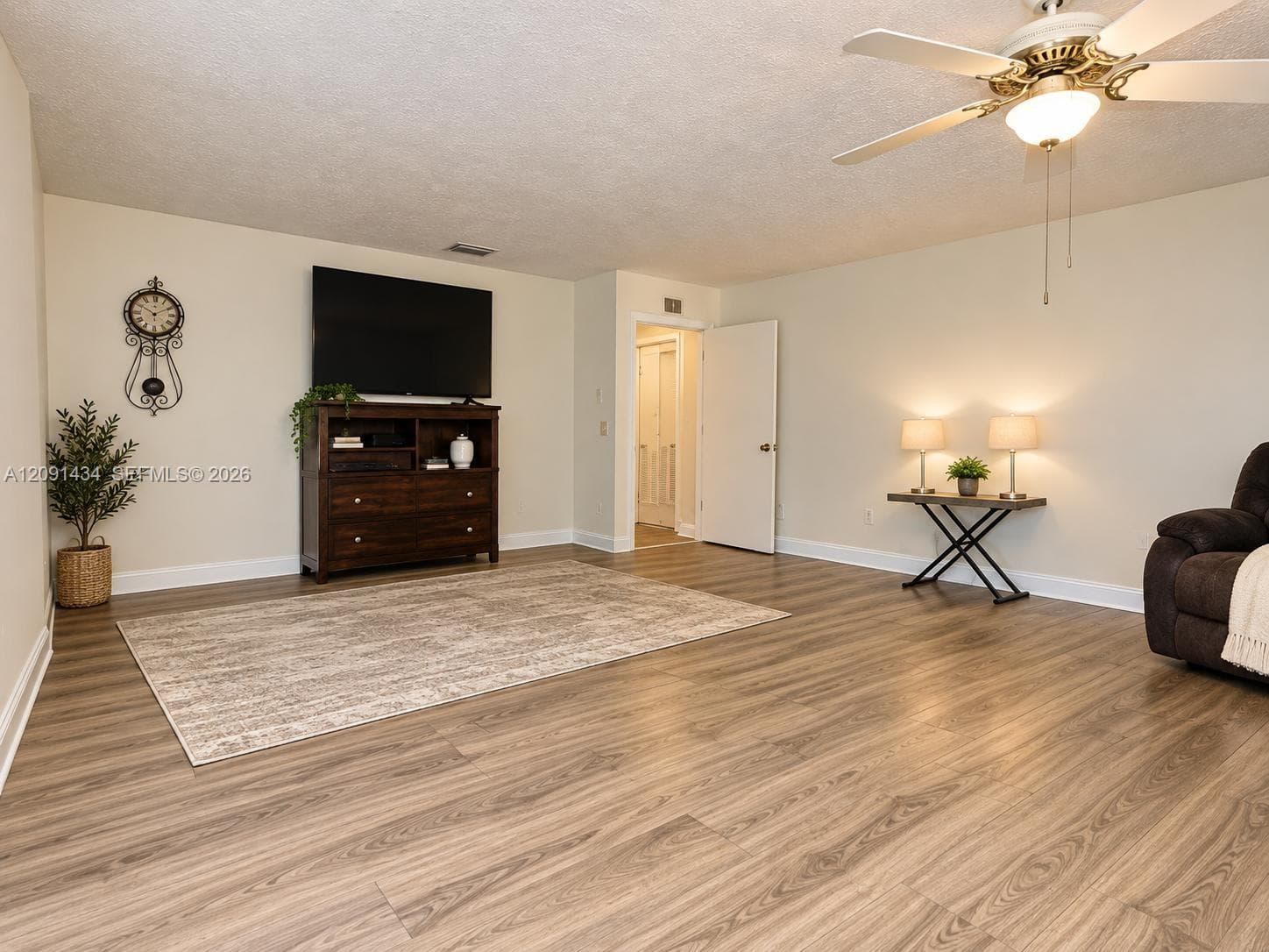 Living area featuring wood-finish flooring, a neutral color palette, and a multi-blade ceiling fan with integrated lighting