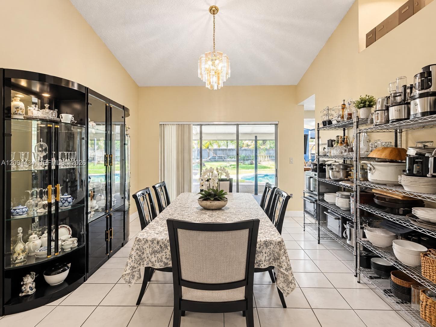 Vaulted ceiling featuring a tiered crystal chandelier, expansive tile flooring, and floor-to-ceiling sliding glass doors