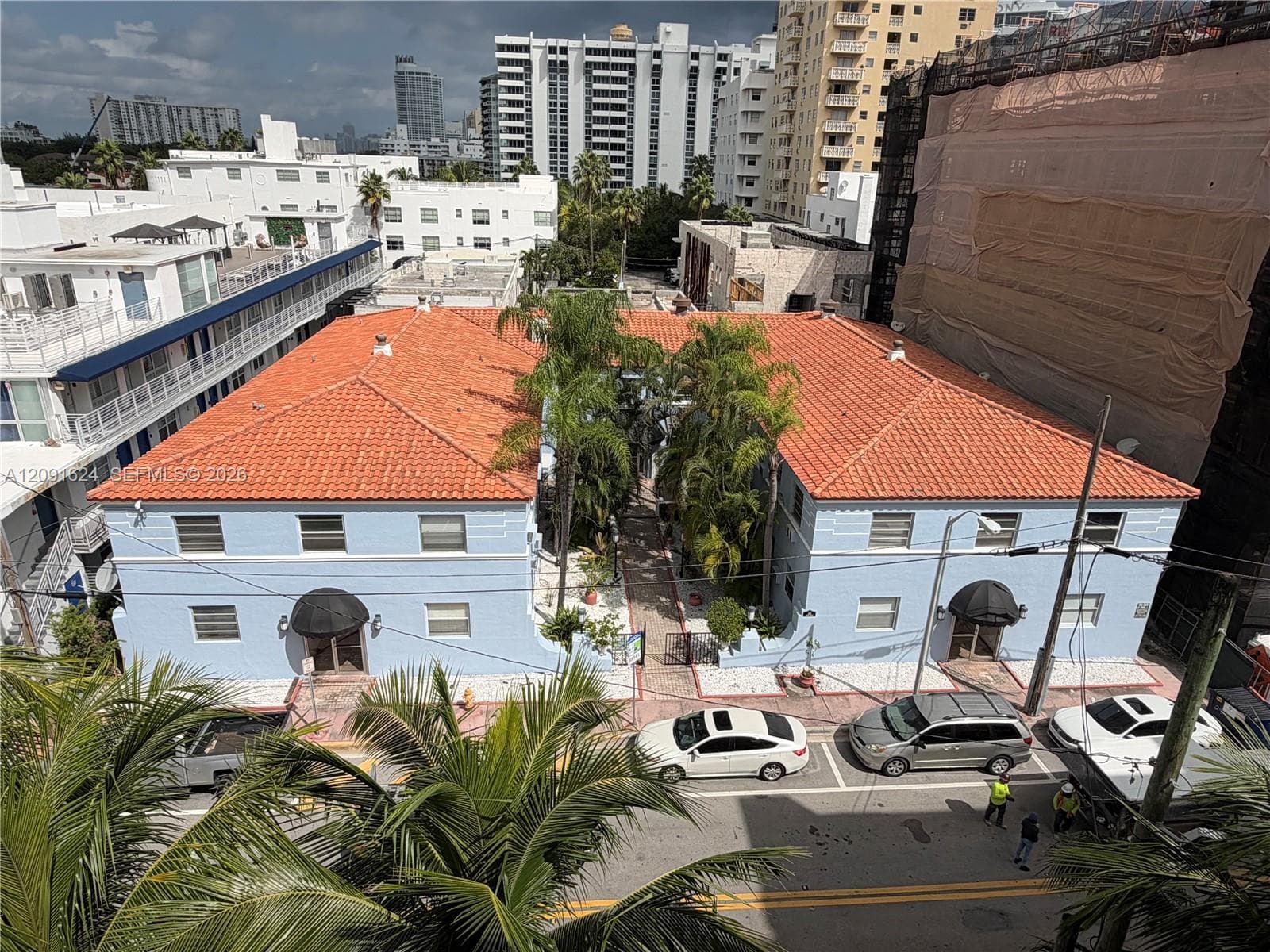 Two-story exterior featuring a clay tile roof, light blue facade with horizontal molding detail, arched entryways with black awnings, and a central landscaped courtyard