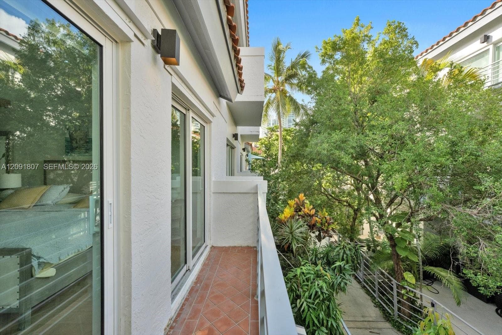 Exterior balcony featuring terracotta tile flooring, metal railing, stucco wall finish, and wall-mounted exterior lighting