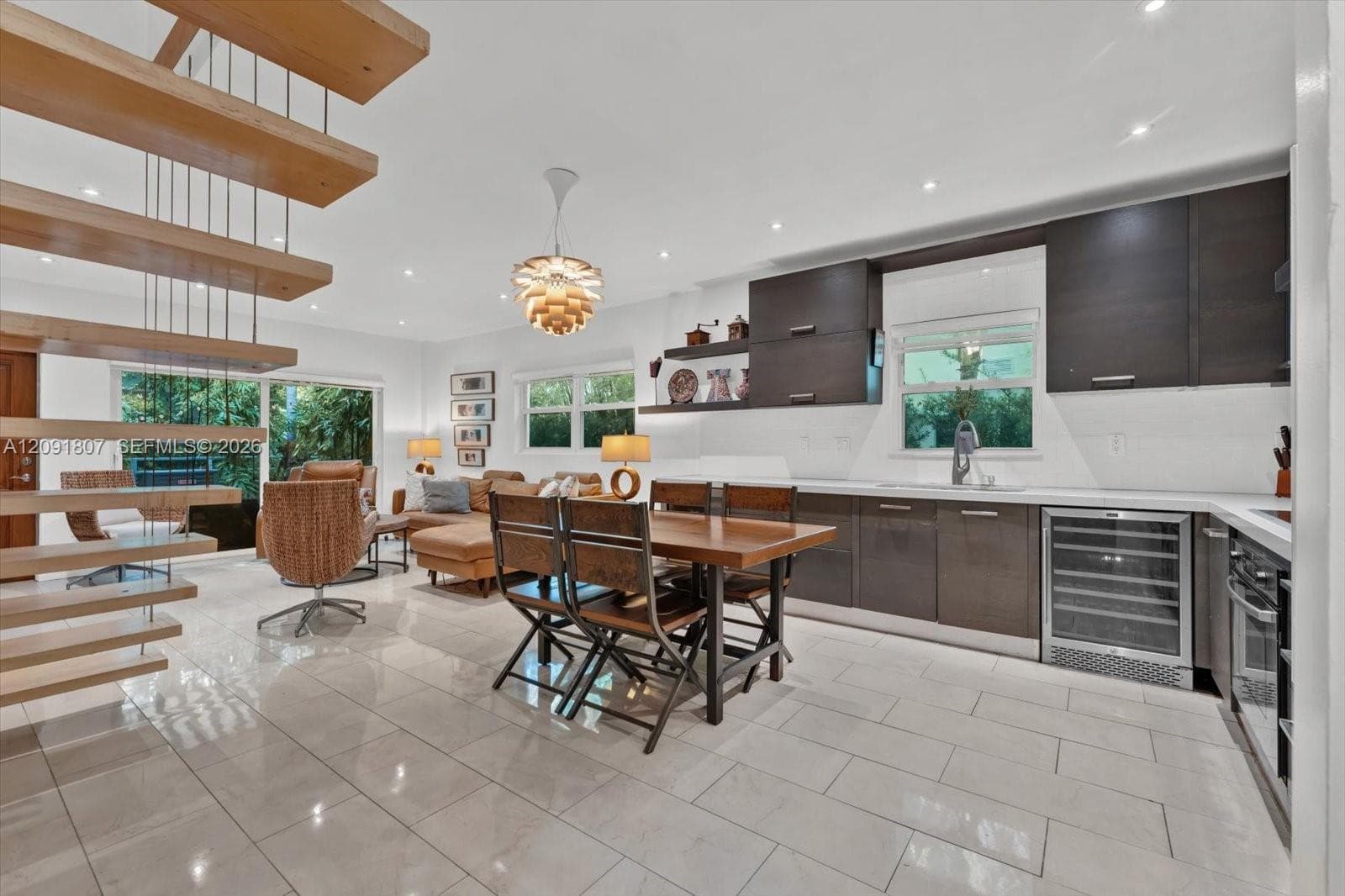 Open-concept kitchen and living area featuring a floating staircase with wood treads, high-gloss cabinetry, built-in wine refrigeration, large-format tile flooring, and recessed ceiling lighting