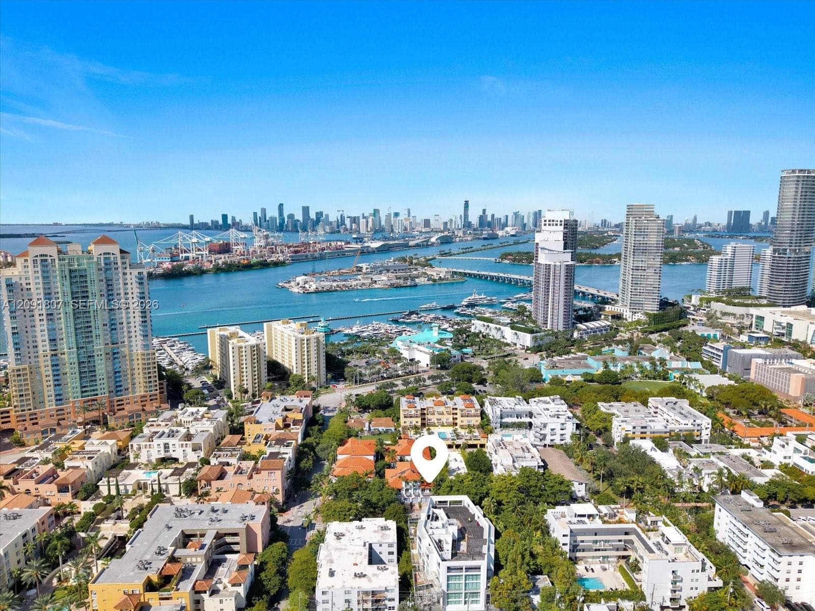 Aerial perspective of the coastal cityscape featuring a prominent skyline, expansive waterway, marinas, high-rise architecture, and mature canopy foliage