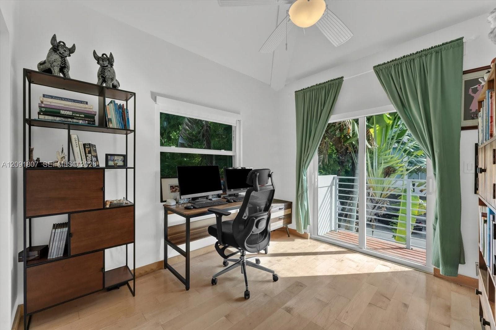 Room featuring light wood-finish flooring, a vaulted ceiling with a central integrated light fixture, a double-pane window, and a sliding glass door providing access to a railed balcony