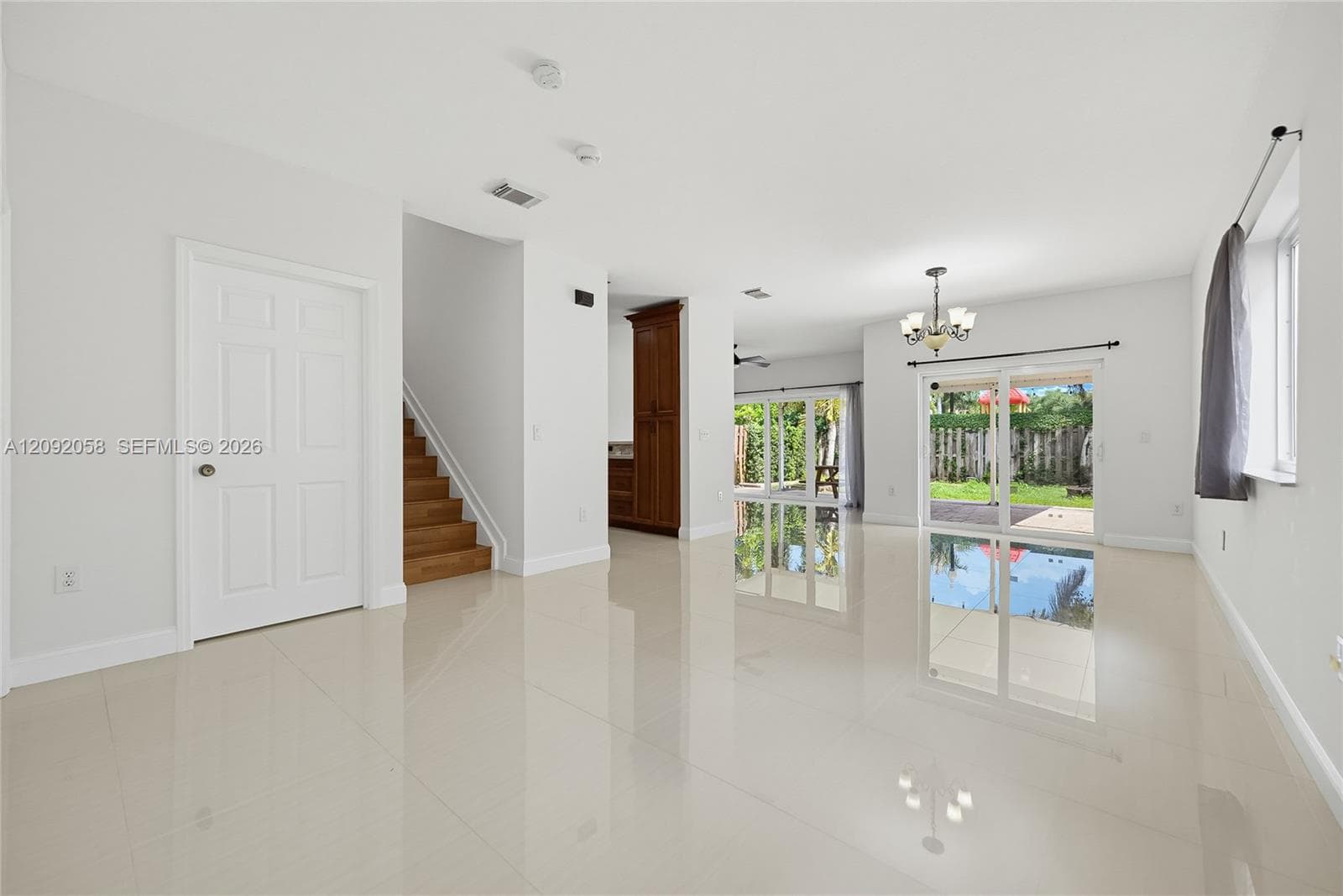 Large-format tile flooring, wood-finish staircase, built-in cabinetry, multi-light chandelier, and glass sliding doors