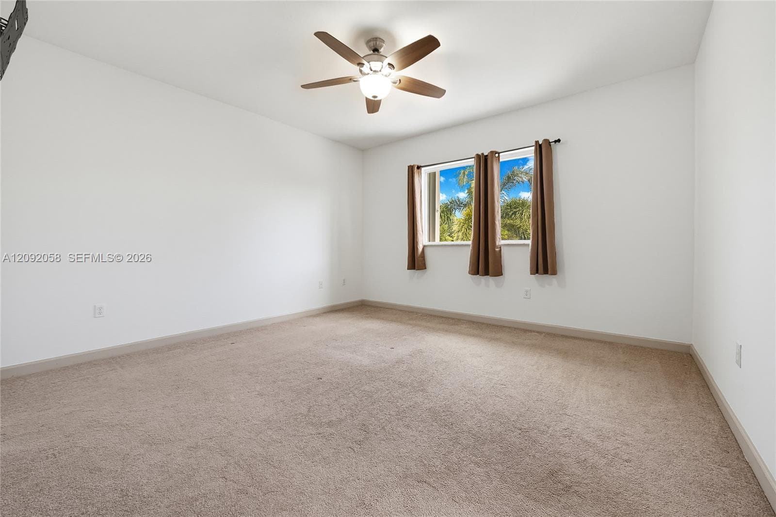 Neutral interior space featuring wall-to-wall carpeting, high-ceiling mounting for a multi-blade ceiling fan with integrated lighting, and a window with exterior scenery