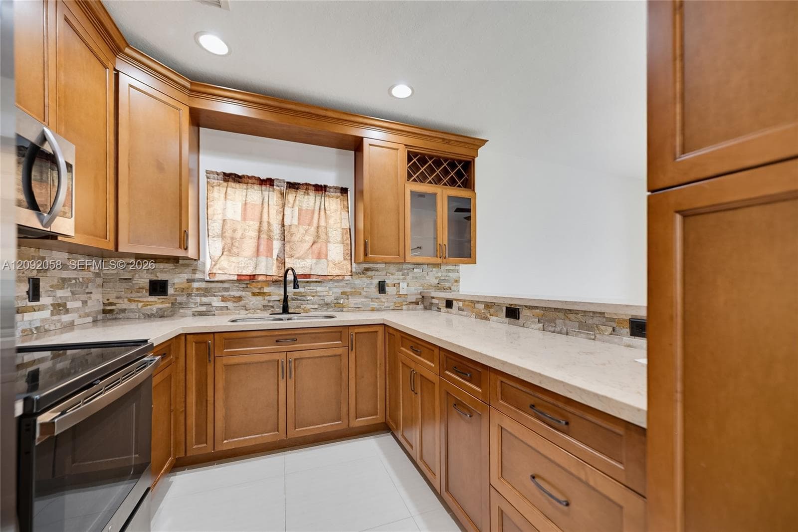 Kitchen featuring wood cabinetry, stone tile backsplash, light-toned countertops, built-in wine rack, and recessed ceiling lighting