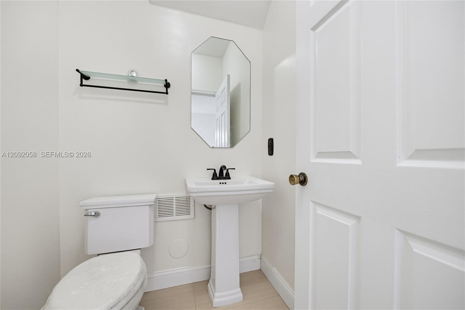 Powder room featuring a pedestal sink, matte black faucet, wall-mounted glass shelving, and an octagonal mirror