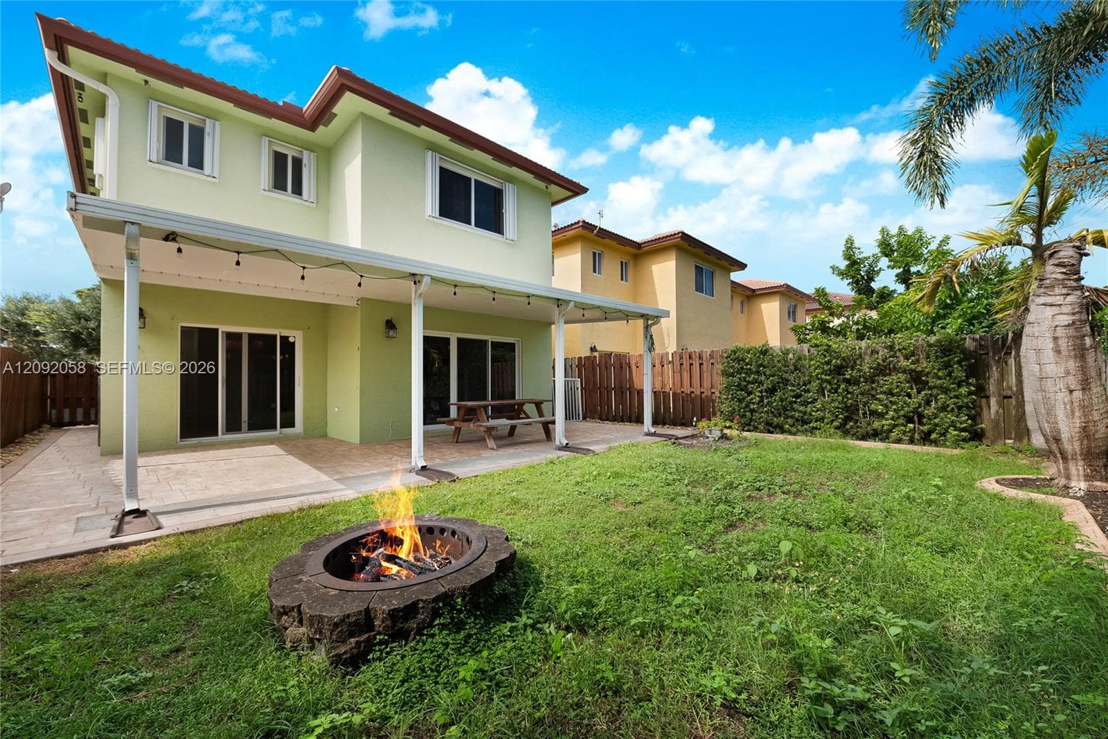 Rear exterior featuring a covered patio, paved hardscaping, a stone-accented fire pit, and a privacy fence