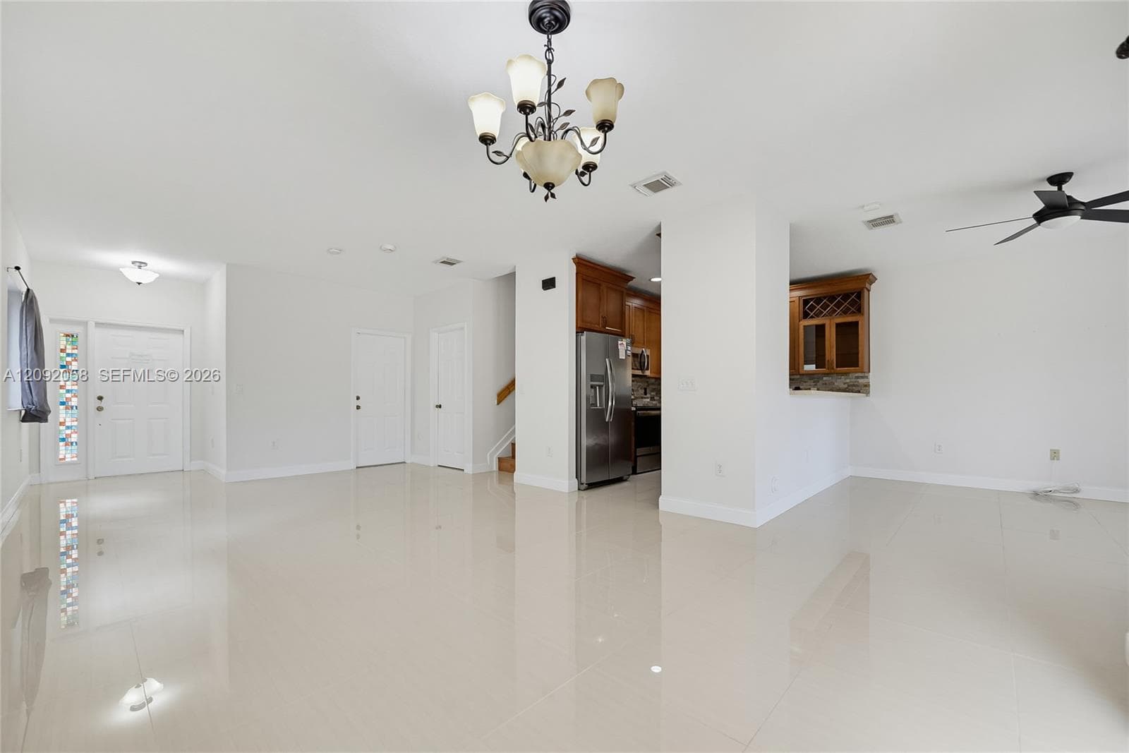 Open-concept interior featuring large-format tile flooring, a multi-light chandelier, a built-in wine rack with glass-front cabinetry, and stainless steel kitchen appliances