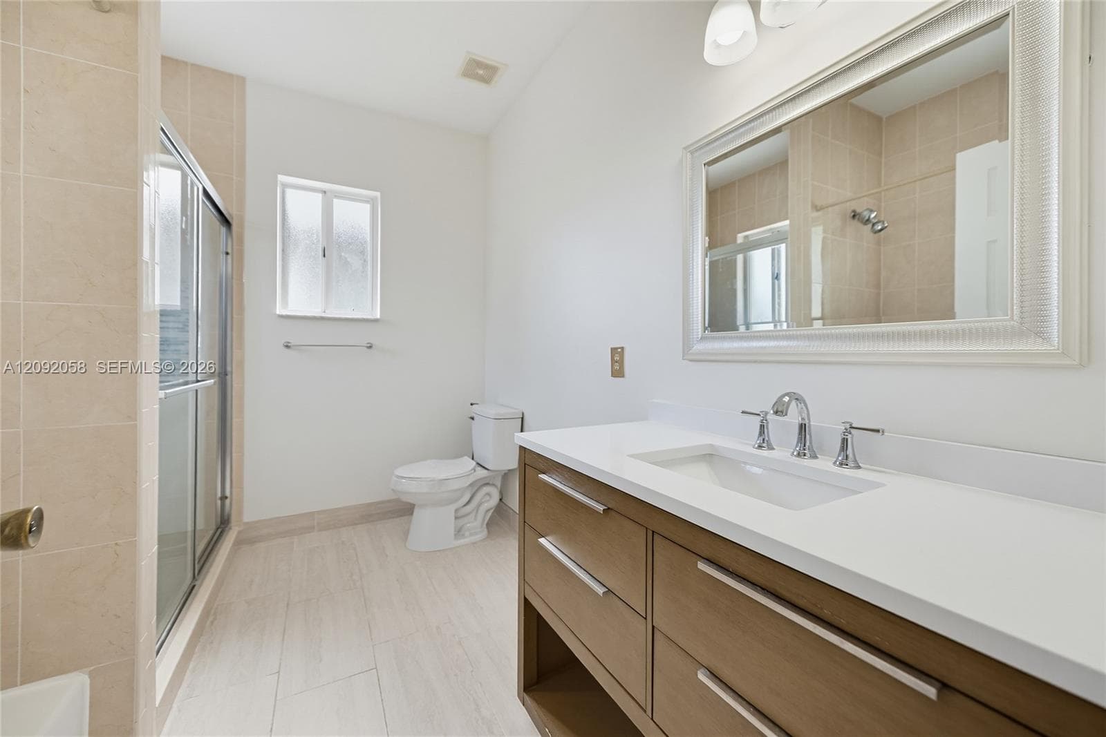 Bathroom featuring a wood-finish vanity with a stone countertop, an integrated sink, a framed wall mirror, and a glass-enclosed shower with tiled walls