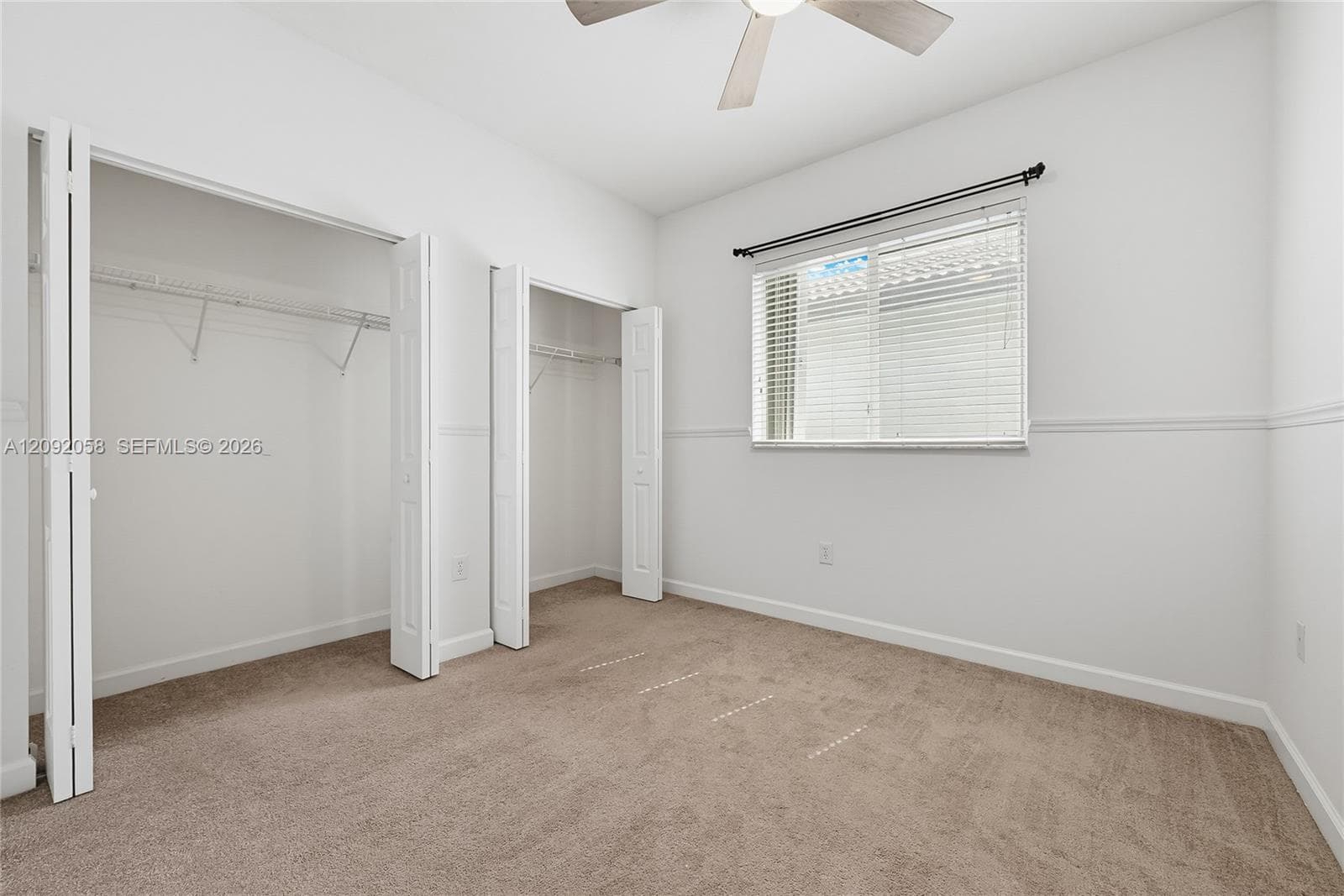 Neutral-toned wall-to-wall carpeting, dual closets with bi-fold doors, white chair rail molding, ceiling fan with integrated lighting, and horizontal blinds